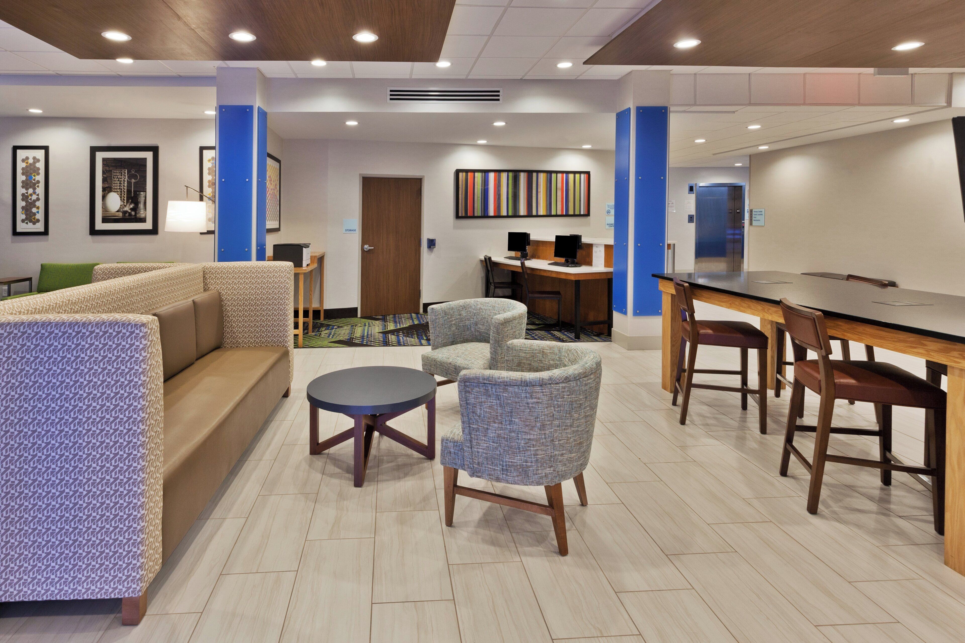 Eine Hotellobby mit einer Couch, Sesseln, einem kleinen Tisch, einem Schreibtisch mit Computern und einer Rezeption.