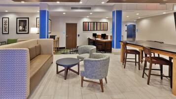 Eine Hotellobby mit einer Couch, Sesseln, einem kleinen Tisch, einem Schreibtisch mit Computern und einer Rezeption.