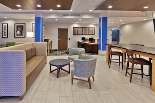 Un hall de hotel con un sofá, sillones, una pequeña mesa, un escritorio con computadoras y una zona de recepción.