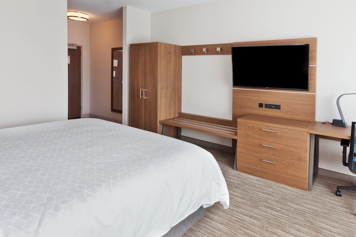 Habitación de hotel con una cama grande, un escritorio de madera, un televisor de pantalla plana, un armario y una lámpara de escritorio.