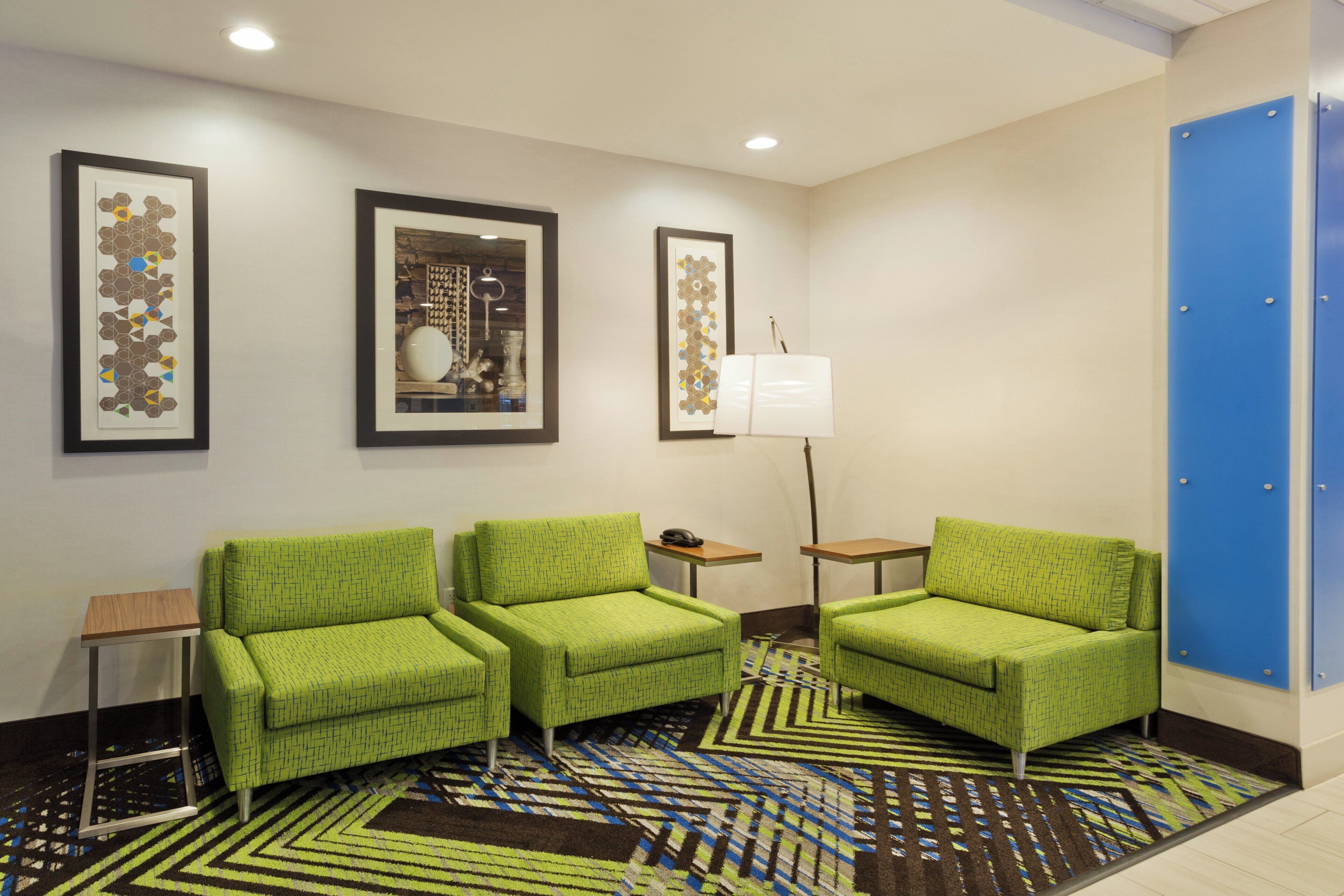 A hotel lobby with green armchairs, a patterned carpet, and framed artwork on the walls.