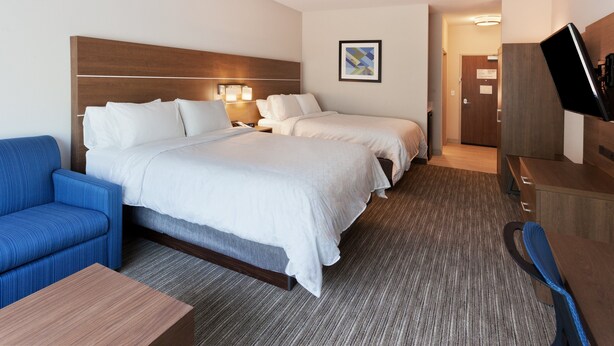 A hotel room with two beds, a blue armchair, a wooden desk, and a television. - Holiday Inn Express & Suites Fayetteville by IHG (Fayetteville)