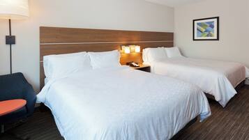 A hotel room with two beds, a desk, a chair, a lamp, and a wall-mounted artwork.