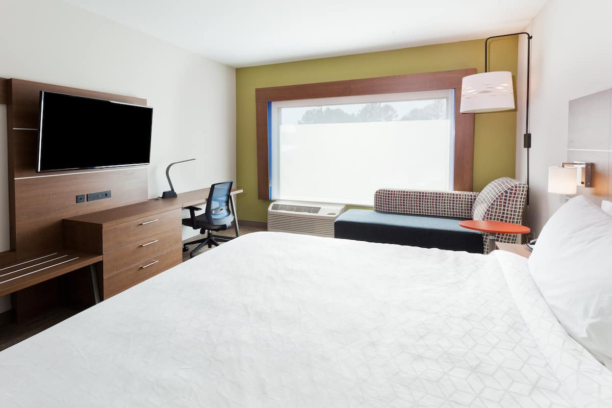 Habitación de hotel con cama, escritorio con silla, televisor y ventana con vistas.