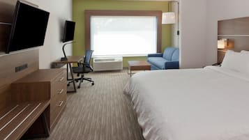 A hotel room with a bed, a desk with a chair, a TV mounted on the wall, and a large window.
