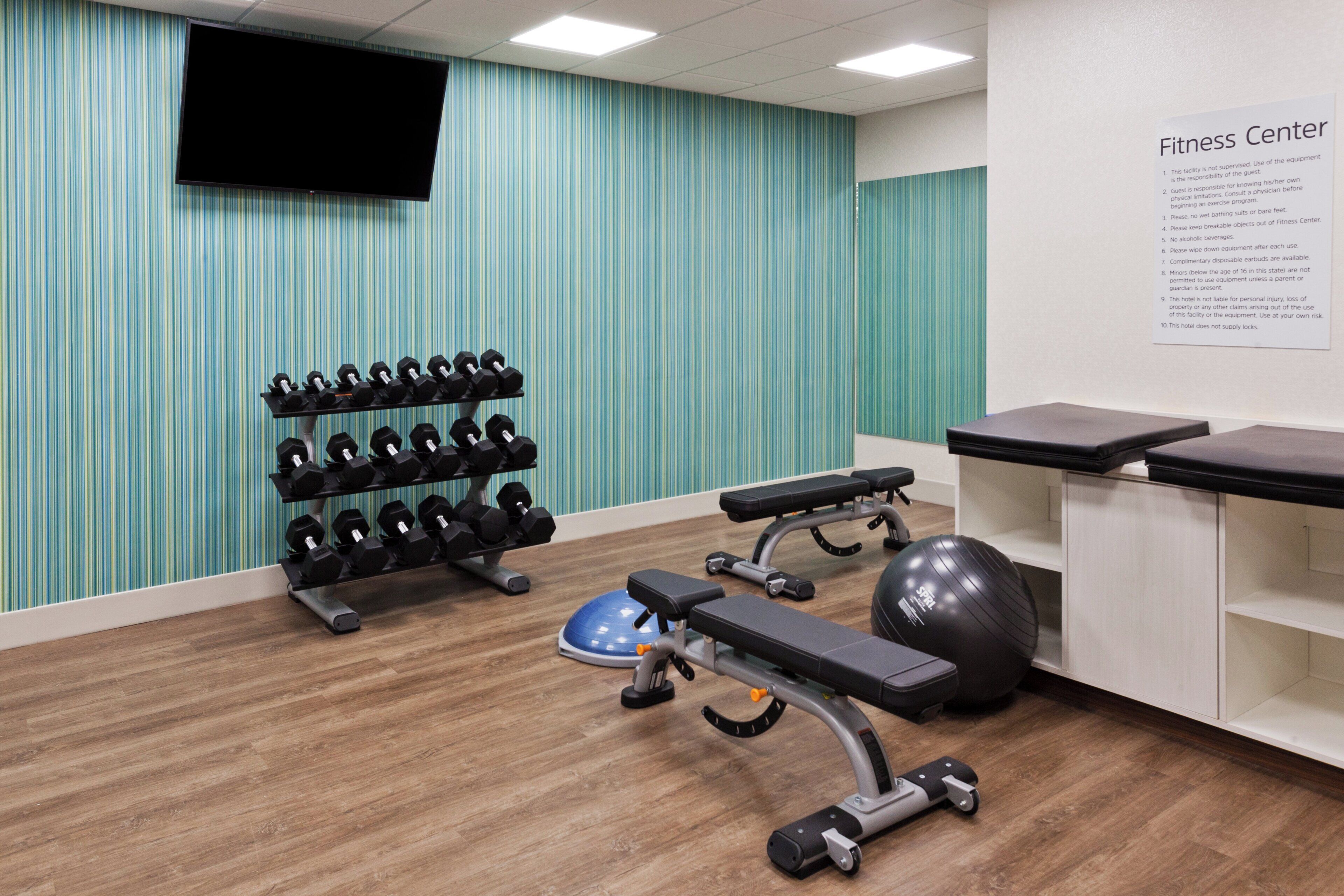 A fitness center with exercise equipment, a wall-mounted TV, and a sign listing rules and regulations.