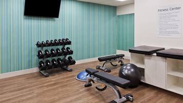 A fitness center with exercise equipment, a wall-mounted TV, and a sign listing rules and regulations.