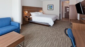 A hotel room with a bed, a blue sofa, a desk, a TV, and a wooden wardrobe. - Holiday Inn Express & Suites Fayetteville by IHG (Fayetteville)