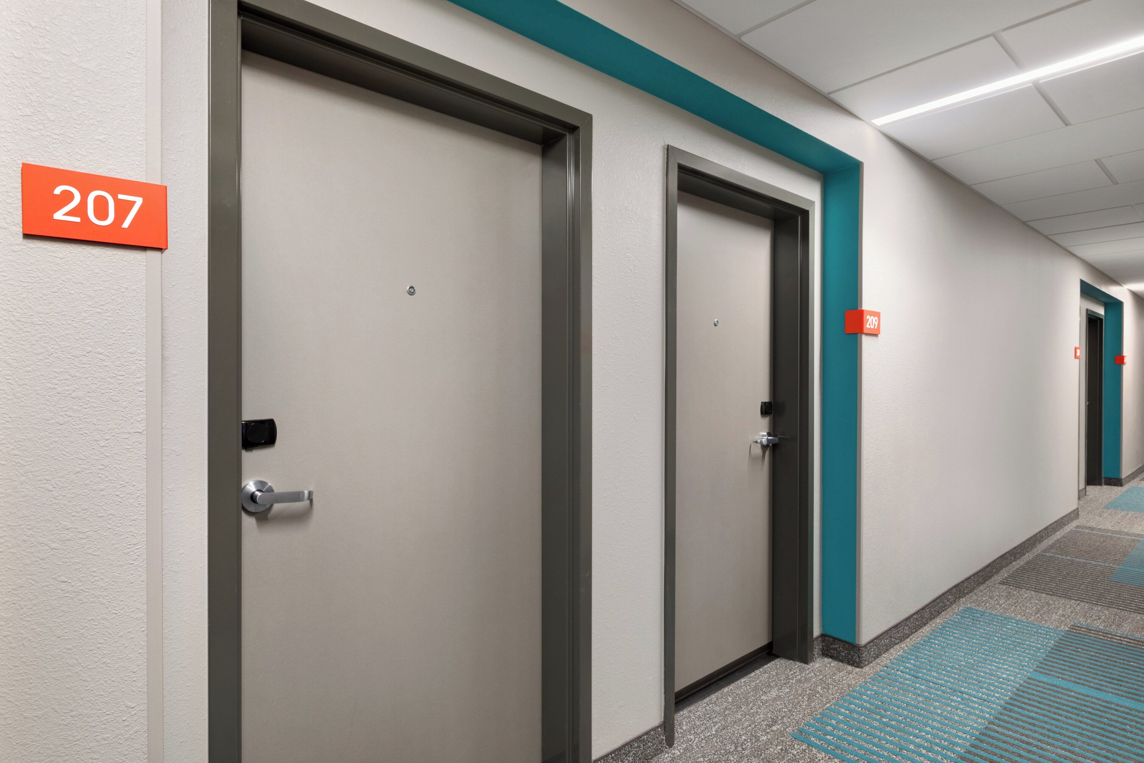 A corridor with doors numbered 207 and 209, carpeted flooring, and a ceiling with recessed lighting.