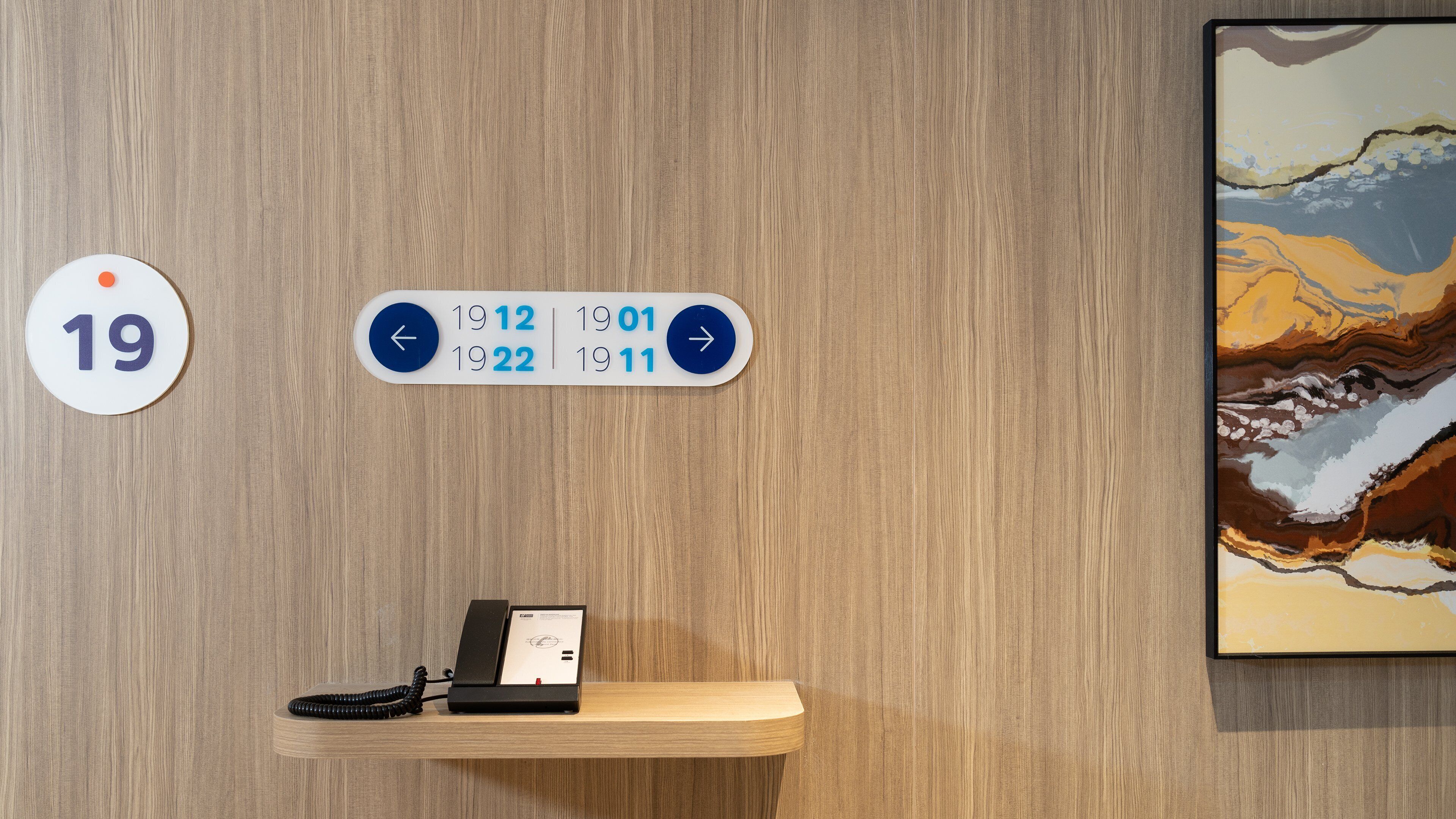 A hotel reception area with a wooden wall, a reception desk, a phone, and a wall clock displaying the time.