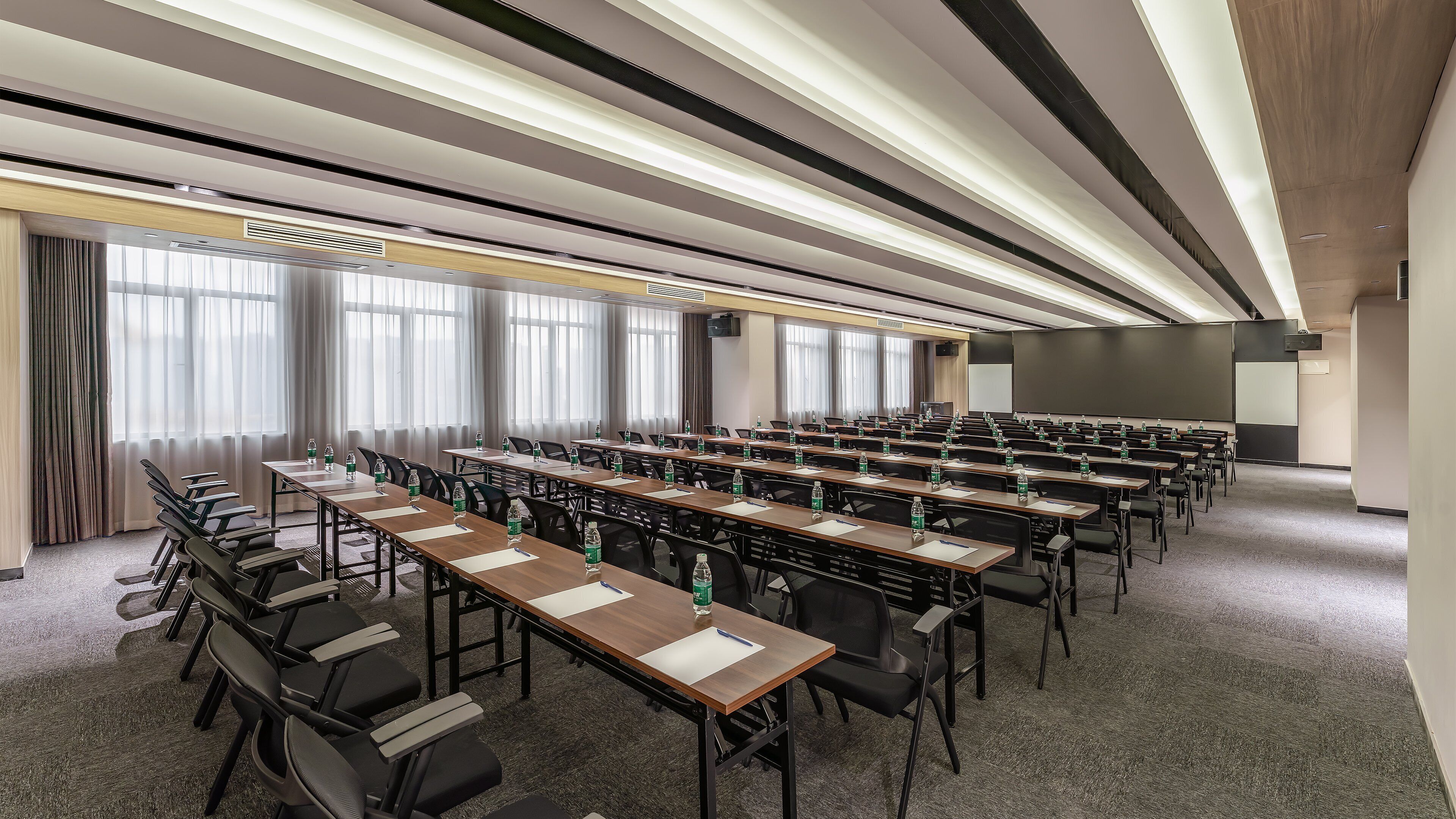 Un salón de conferencias con filas de mesas, sillas y una pantalla para proyector.