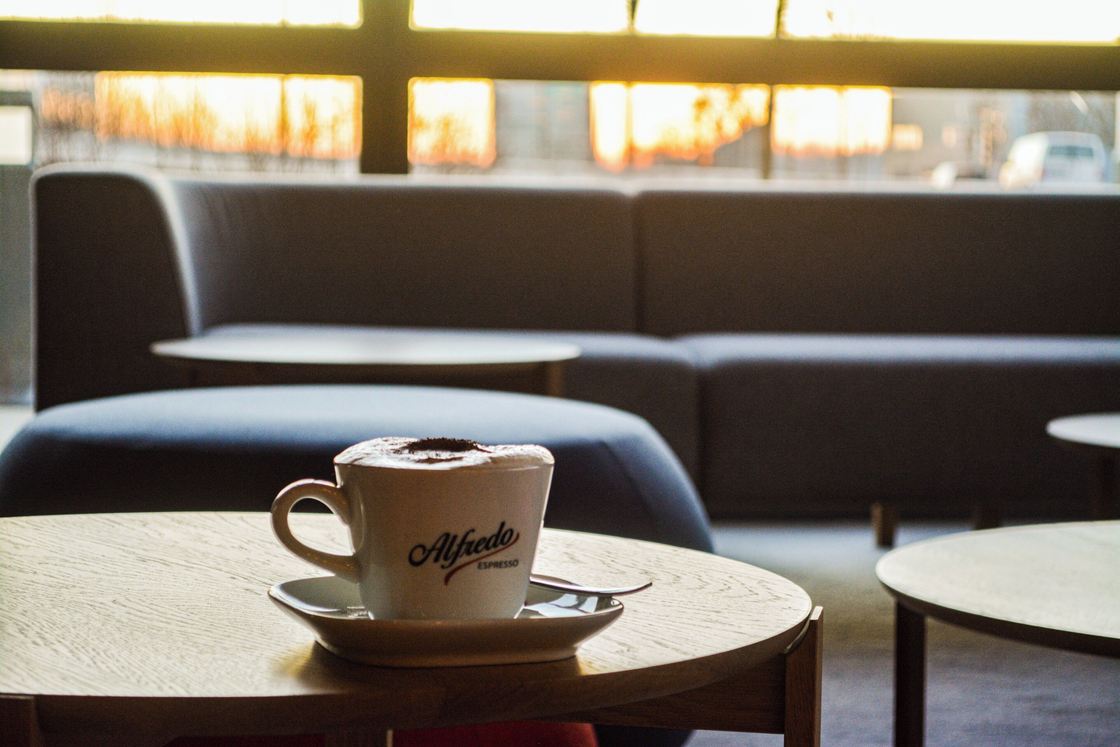 Eine Tasse Kaffee auf einem Untertasse mit dem Schriftzug 'Alfredo' auf einem Tisch in einem Café.