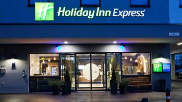 The exterior of a Holiday Inn Express hotel with a glass entrance, outdoor seating, and a visible sign.