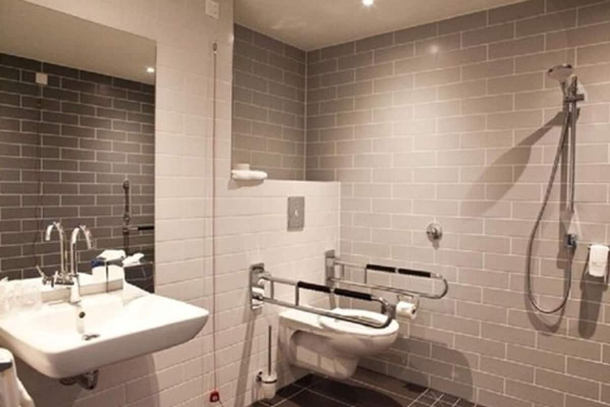A modern bathroom with a white sink, a toilet with a safety rail, and a shower area.