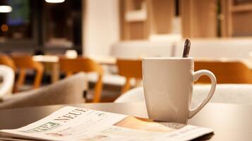 A white cup on a tray with a spoon, a newspaper, and a table in a cafe setting.