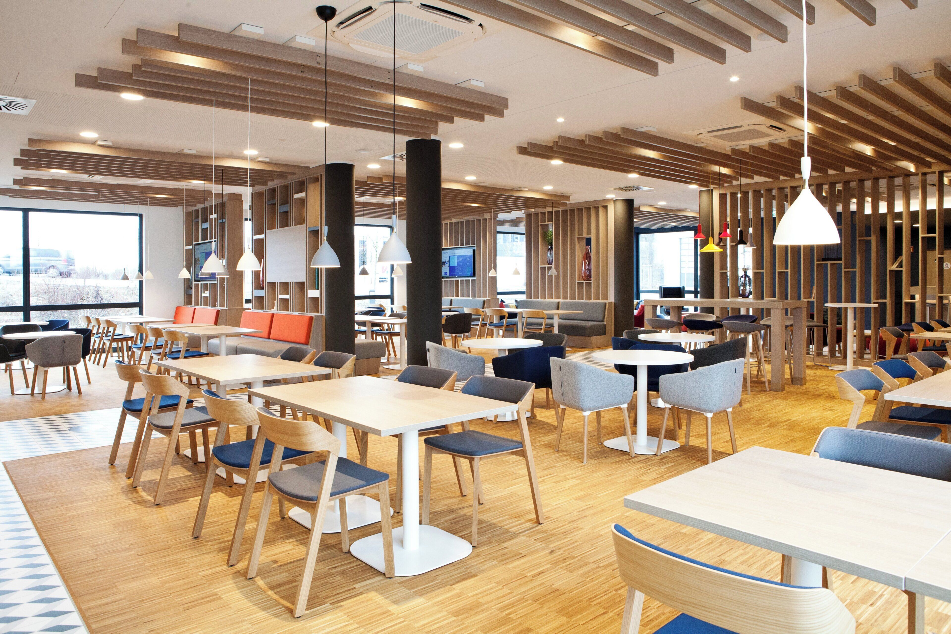 A modern dining area with wooden tables and chairs, pendant lighting, and a view of the city through large windows.