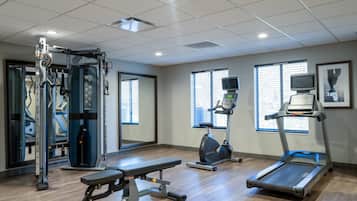 Une salle de sport équipée de machines de cardio, de matériel d’entraînement en force et dotée de grandes fenêtres.