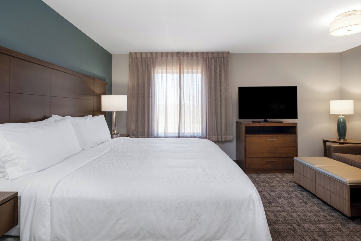 Habitación de hotel con una cama grande, televisión, escritorio y ventana con cortinas.