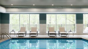 A swimming pool with four lounge chairs and a metal ladder, surrounded by large windows with a view of trees. - Staybridge Suites Sioux City Southeast by IHG (Sioux City)