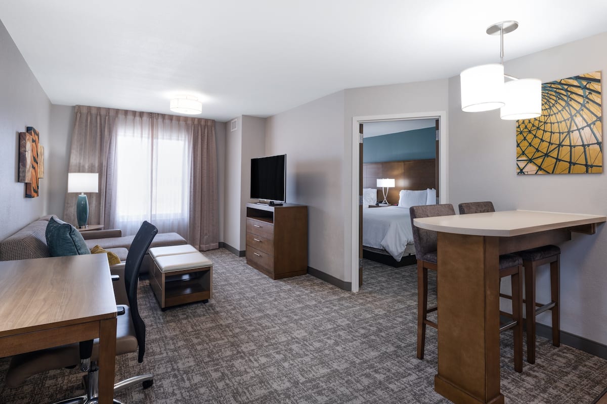 A hotel room with a bed, a TV, a desk with a chair, a sofa, and a dining table.