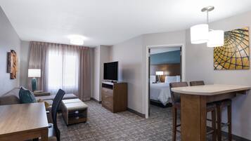 A hotel room with a bed, a TV, a desk with a chair, a sofa, and a dining table.