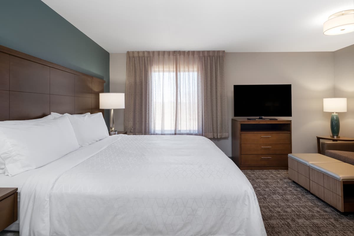 A hotel room with a large bed, a television, a desk, and a window with curtains.