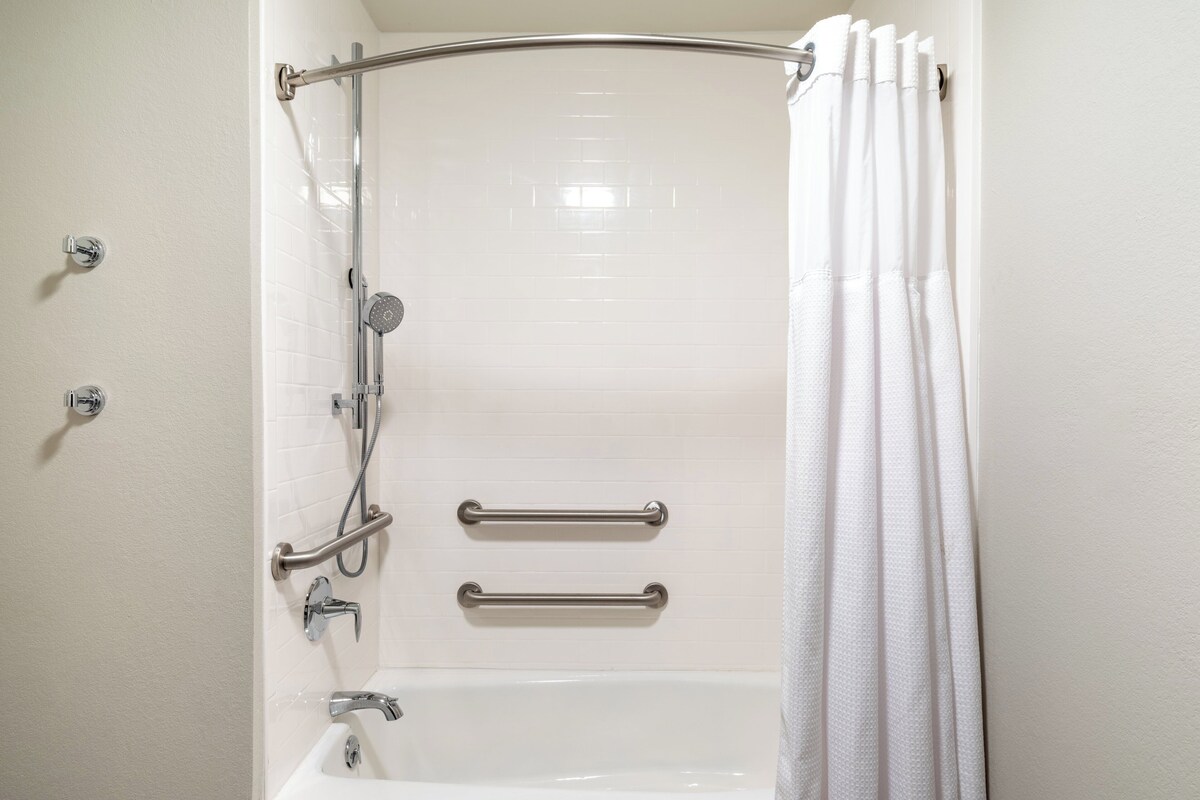 Un baño blanco con ducha, barras de apoyo y bañera.