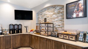 A modern kitchen area with a stone wall, a coffee station, and a glass display case with pastries. - Staybridge Suites Sioux City Southeast by IHG (Sioux City)