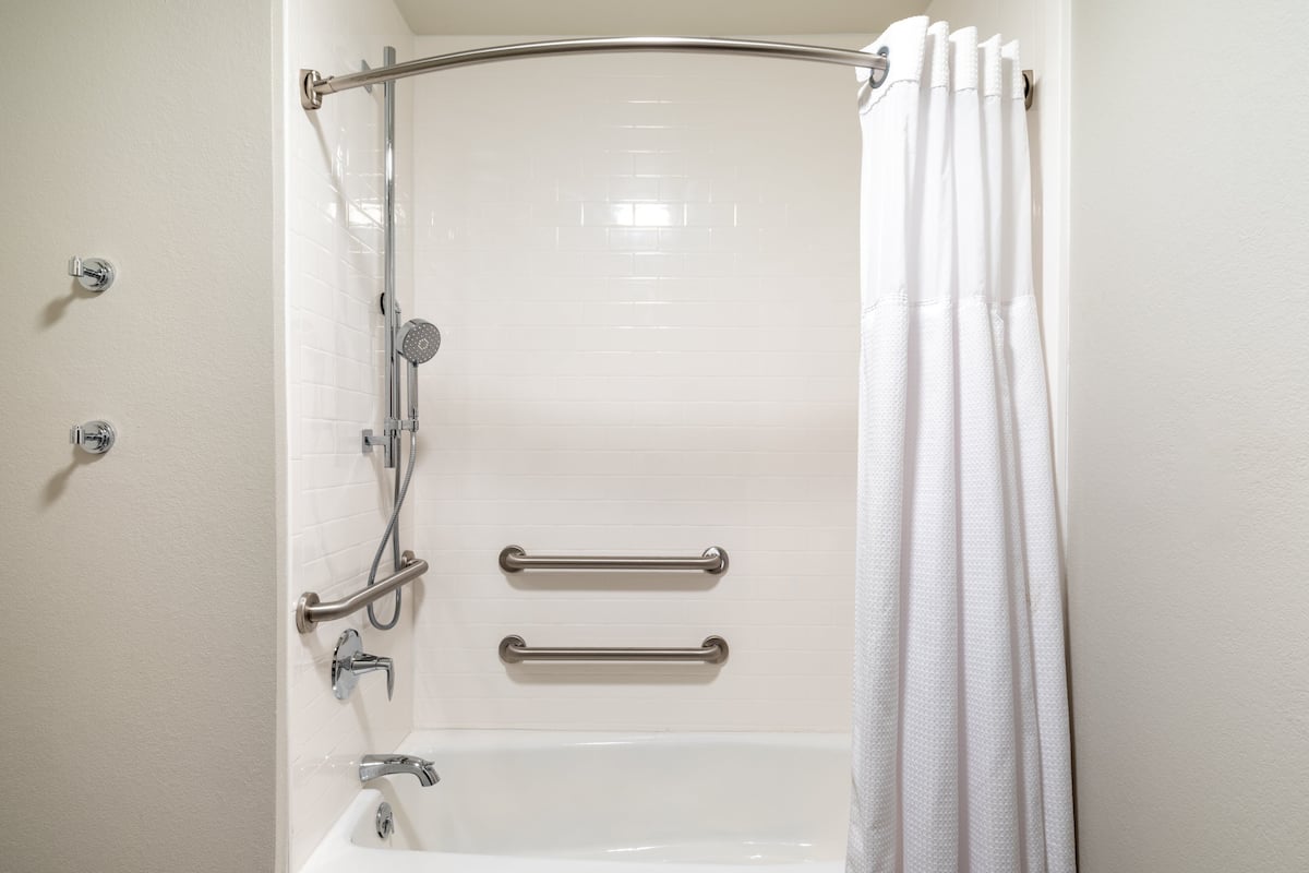A white bathroom with a shower, grab bars, and a bathtub.