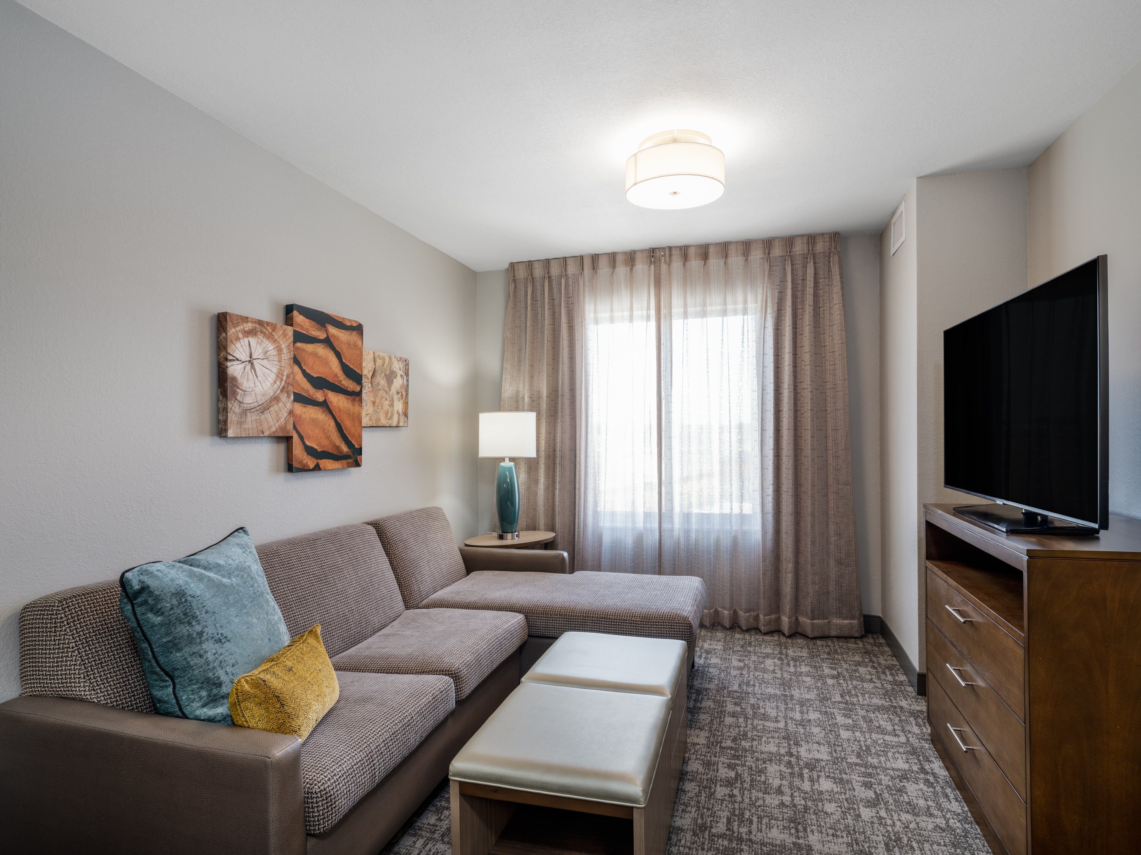A modern hotel room with a sofa, a small table, a TV, and artwork on the wall.