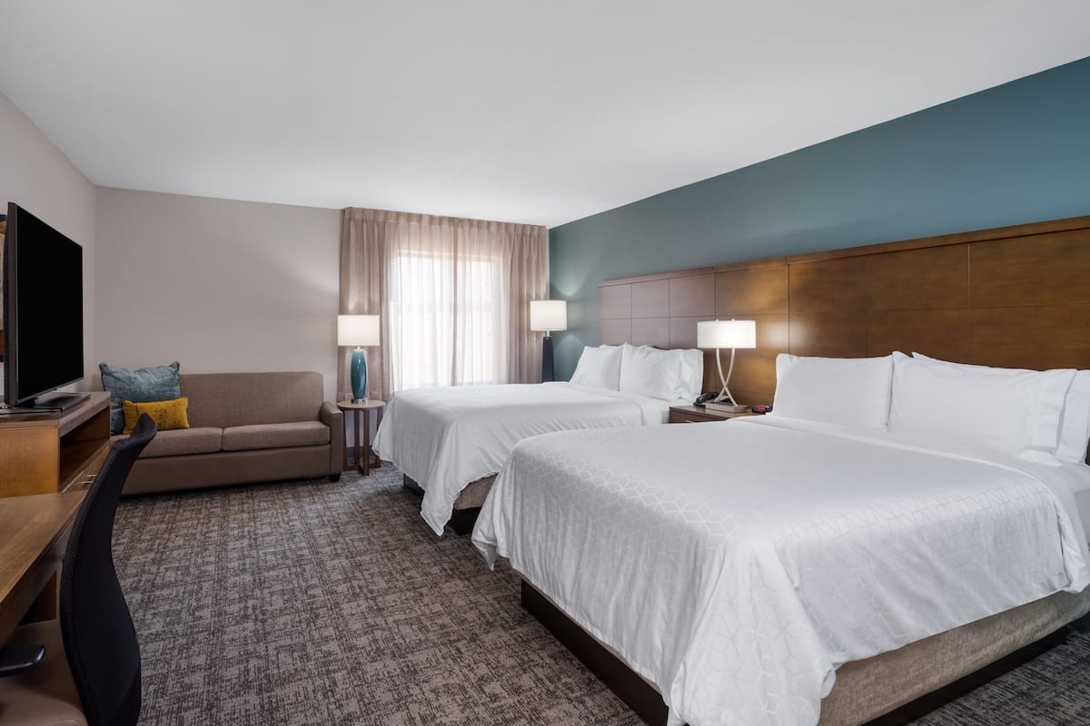 A hotel room with two beds, a TV, a sofa, and a desk.