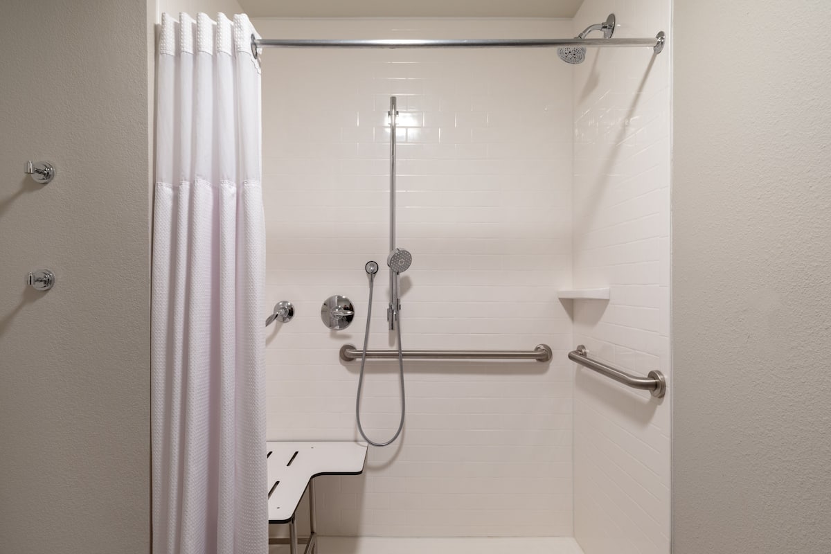A shower with a grab bar, a handheld showerhead, and a handheld faucet.
