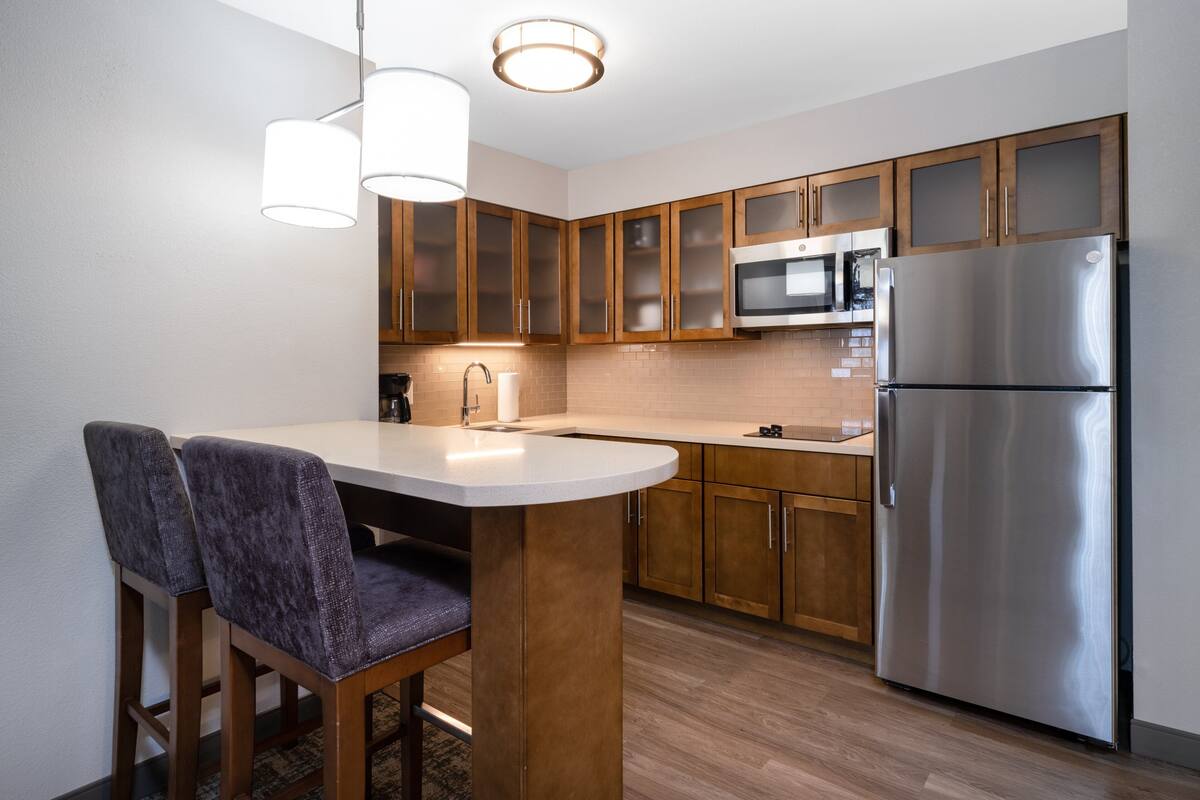 A modern kitchen with wooden cabinets, stainless steel appliances, and a bar stool.