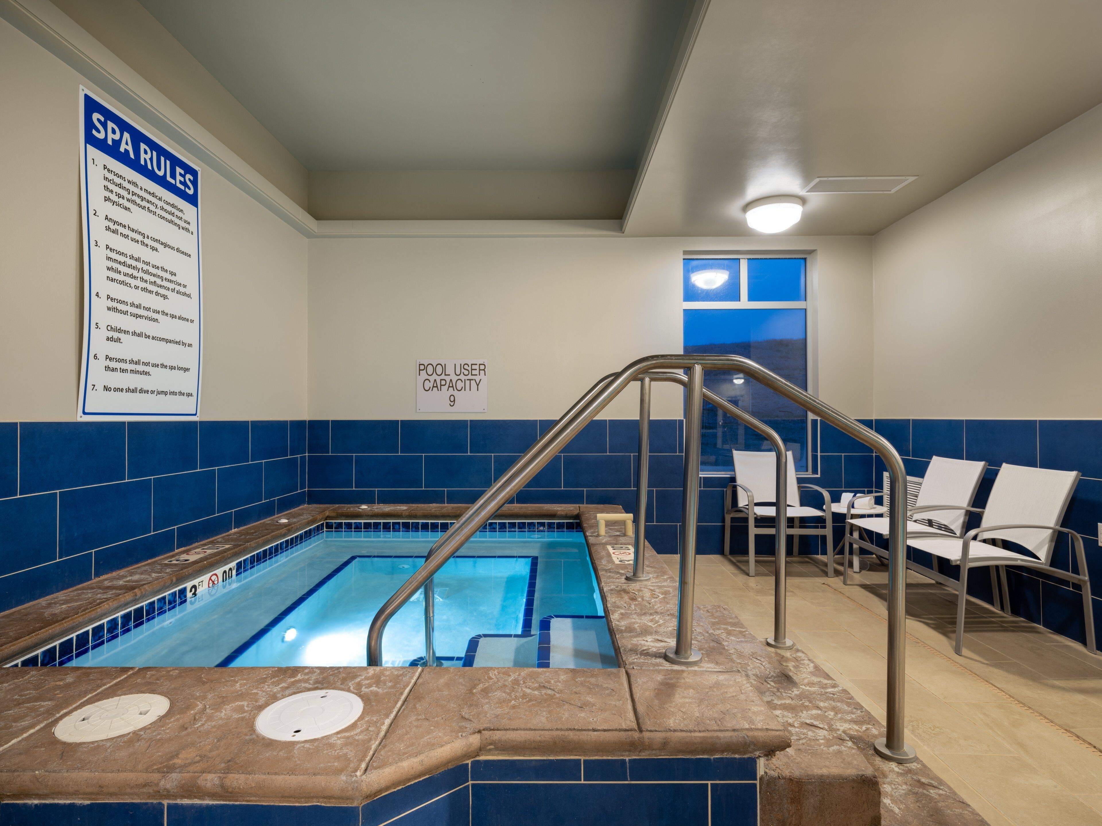 A pool area with a sign listing spa rules, a pool user capacity sign, and a pool with a 3ft depth marker.