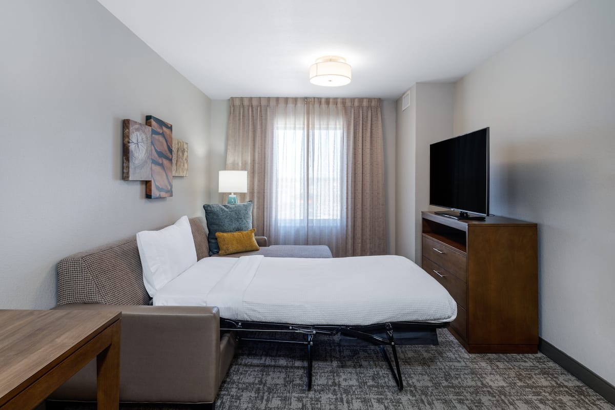 A hotel room with a bed, a desk, a TV, and a window with curtains.