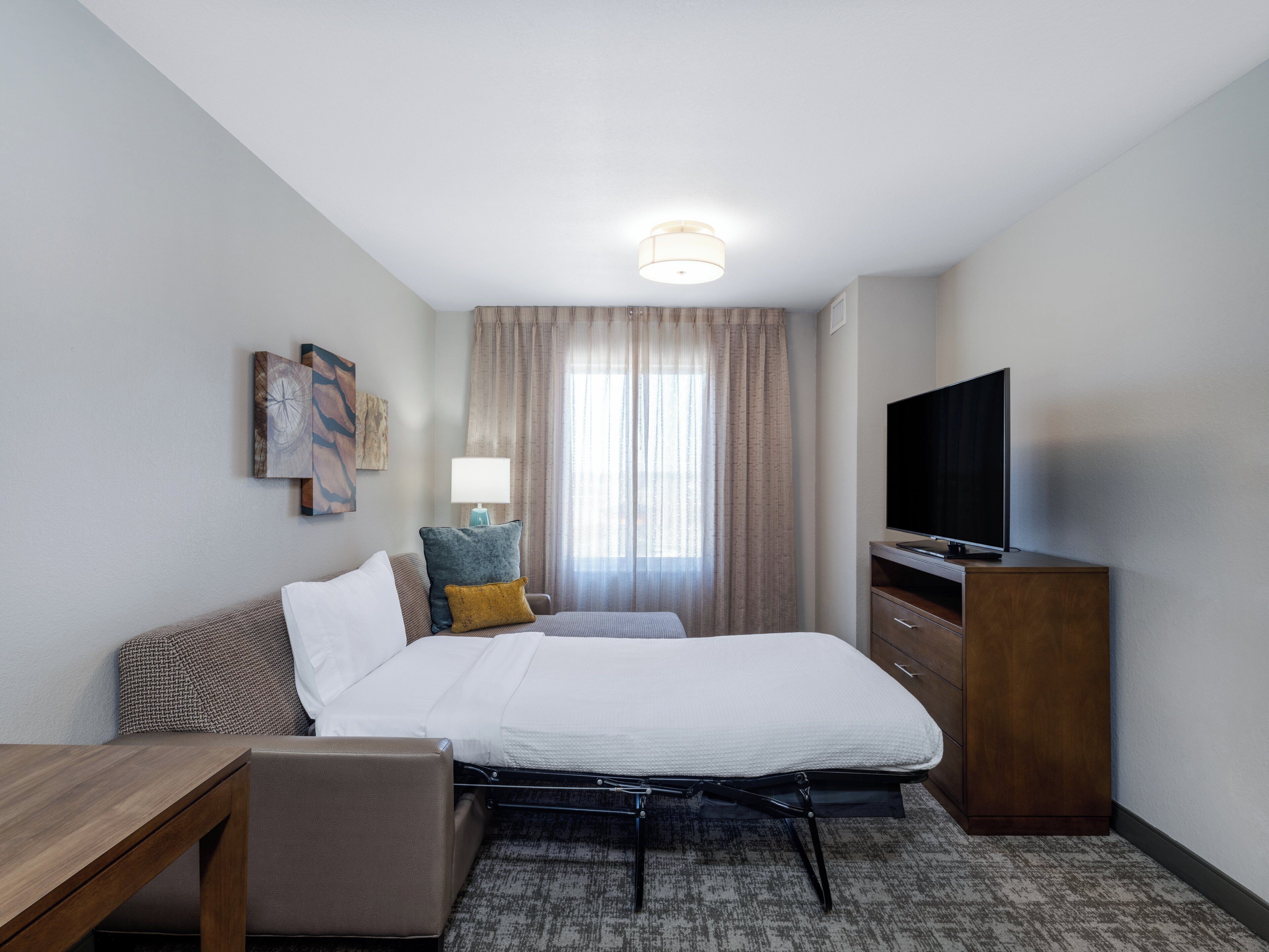 Une chambre d’hôtel avec un lit, un bureau, une télévision et une fenêtre avec des rideaux.