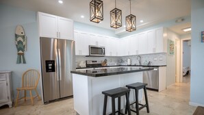 A modern kitchen with white cabinets, stainless steel appliances, a central island with stools, and decorative hanging lights. - ALL DOCKED OUT~ Key Colony Retreat Sandy beach's and sunsets (Key Colony Beach)