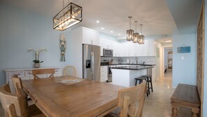 A modern kitchen with white cabinets, stainless steel appliances, and a wooden dining table. - ALL DOCKED OUT~ Key Colony Retreat Sandy beach's and sunsets (Key Colony Beach)