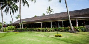 Un hotel con una veranda lunga e coperta, palme e prati curati.