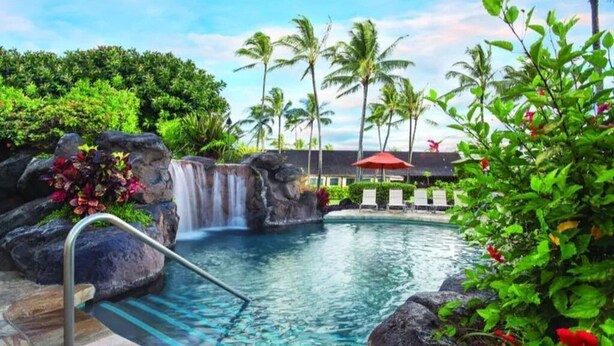 A pool with a waterfall, surrounded by tropical plants and palm trees. - One Bedroom Garden View Kauai Coast Available 12/23-12/30/2025 (Kapaa)