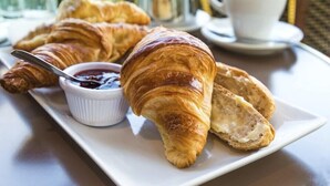 Aamiaistarjoilu, jossa on croissantteja, pieni kulho hilloa ja kuppi kahvia tarjottimella.