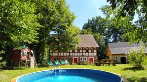 Uma piscina cercada por grama, com uma casa tradicional ao fundo.