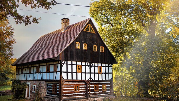Une maison traditionnelle à colombages, dotée d’un toit à forte pente, d’une cheminée bien visible et d’un petit porche.