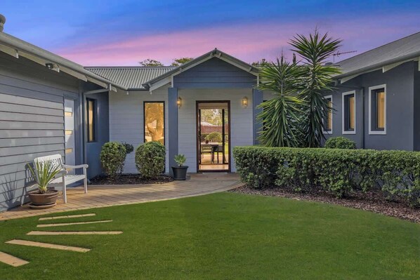 A residential property with a well-maintained lawn, a patio with a bench, and a door leading to a covered outdoor area.