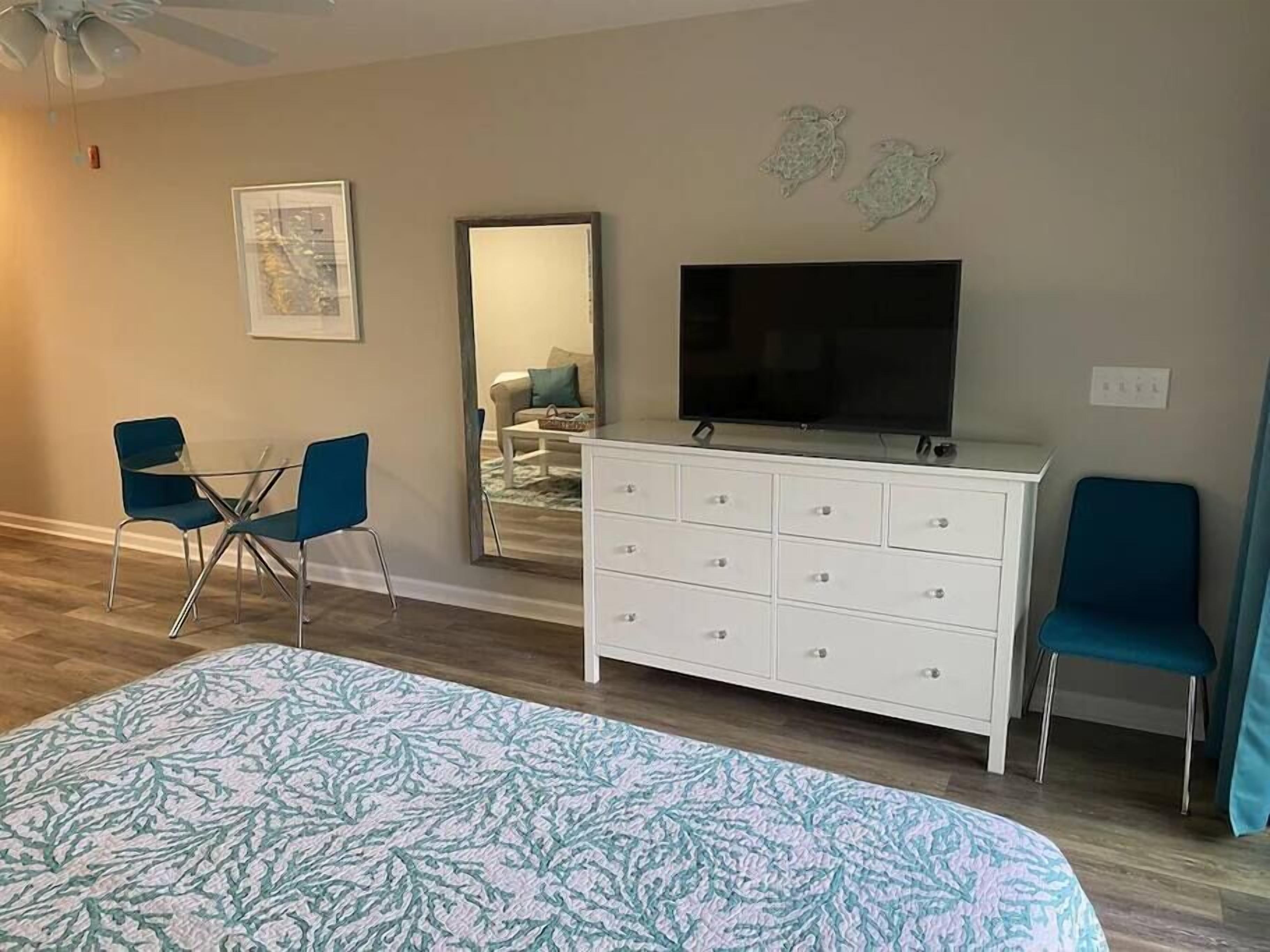 Un dormitorio con cama, televisor, cómoda y dos sillas.