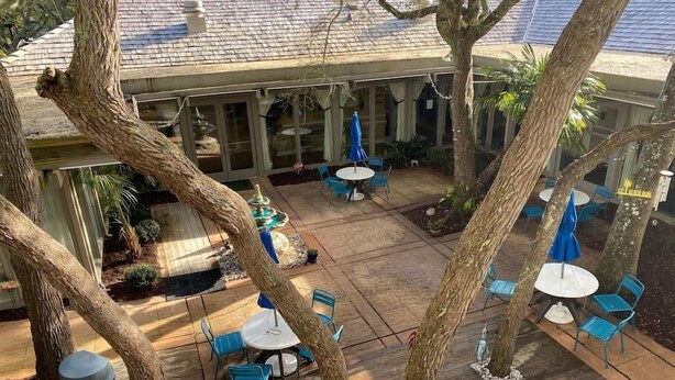 Un patio al aire libre con suelo de madera, sillas y mesas azules, rodeado de árboles.