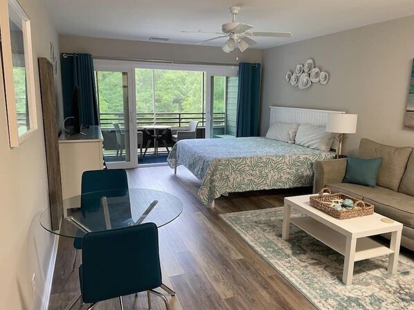 Ein Schlafzimmer mit einem Bett, einem Schlafsofa, einem Couchtisch, einem Glastisch mit Stühlen und einem Balkon mit Tisch und Stühlen.