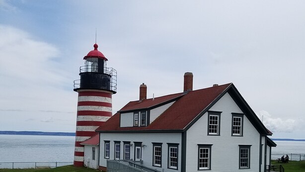 Un faro e un edificio bianco con tetto rosso vicino all'acqua.