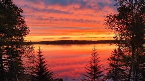 Vista sul lago con un tramonto, alberi e area picnic con sedie e un braciere.