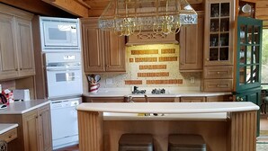 Eine Küche mit Holzausstattung, einer zentralen Kochinsel mit Barhocker, einer Kristallleuchter und einer Spritzschutzwand mit Aufschrift.